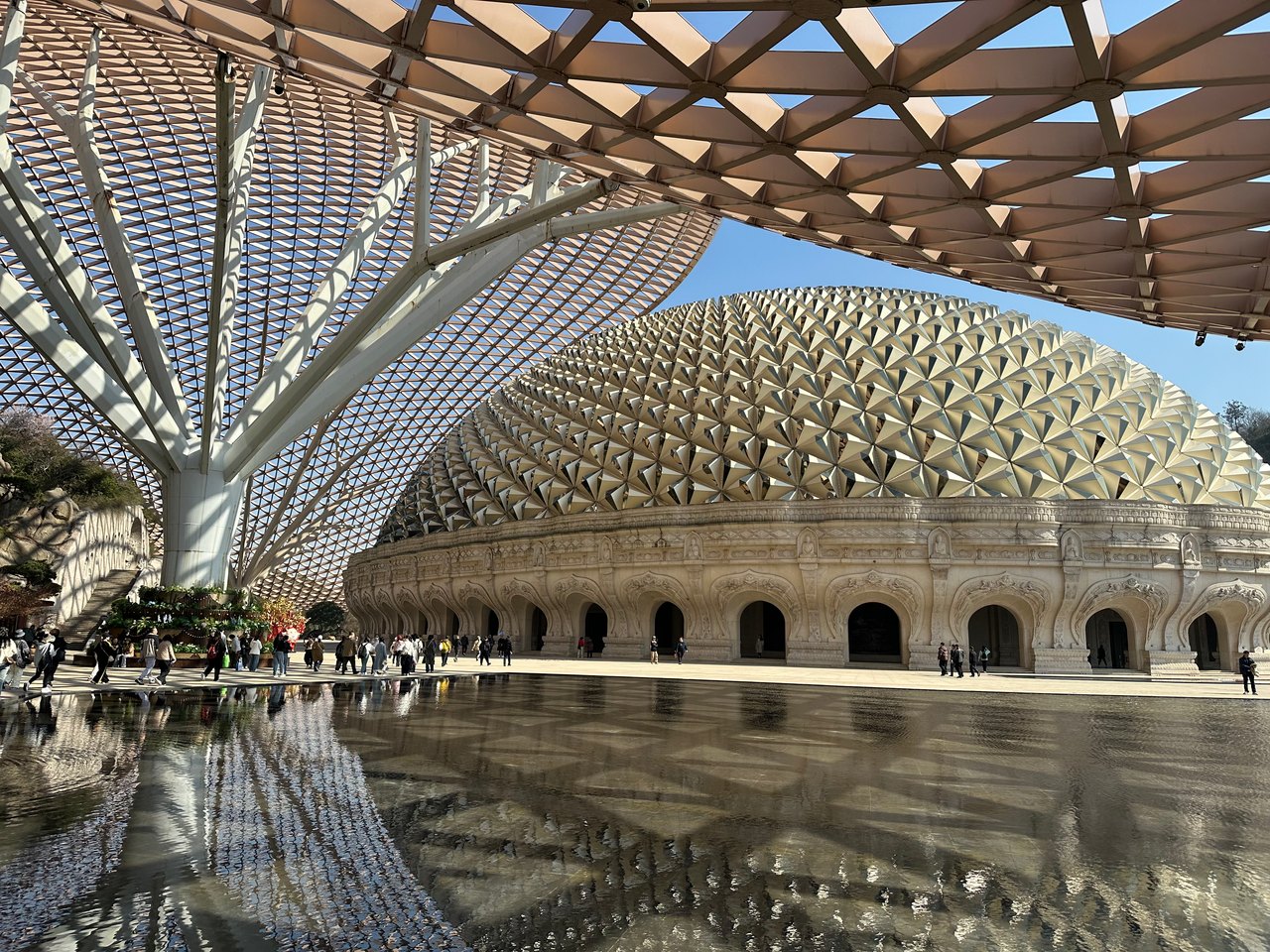 A vast timber lattice roof spans an open hall and reflects in shallow water
