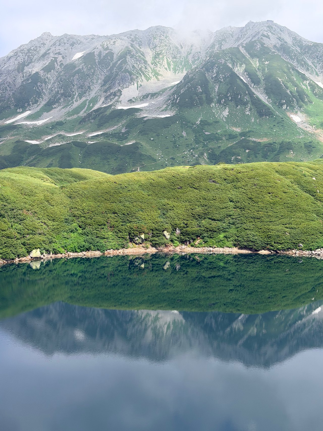 Green slopes and rocky peaks reflected in a still mountain lake