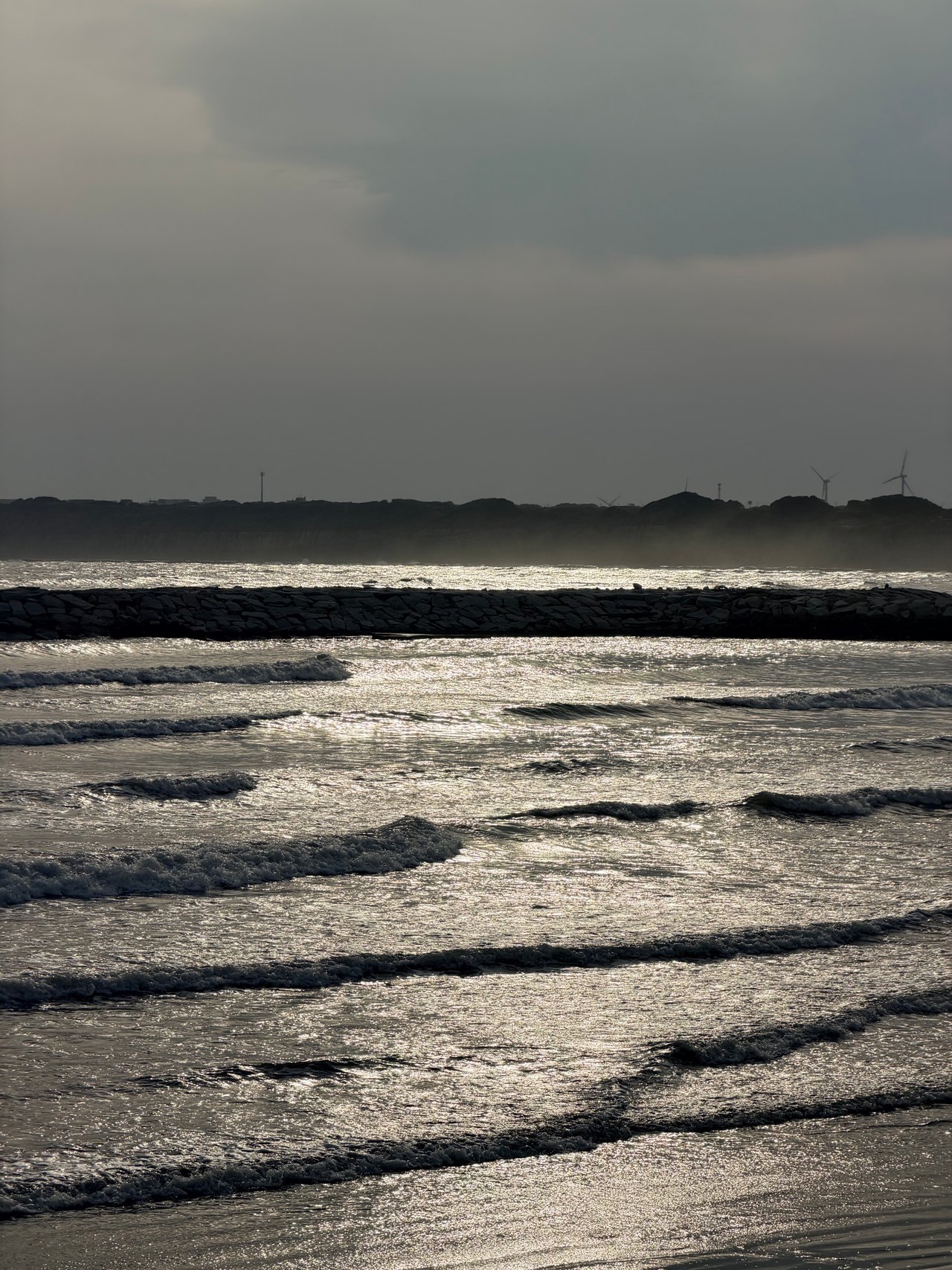 Silver waves form parallel lines toward shore beneath a gray sky
