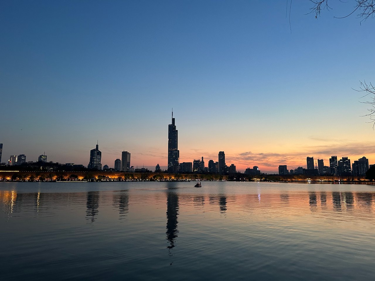A city skyline across calm water beneath an orange and blue evening sky