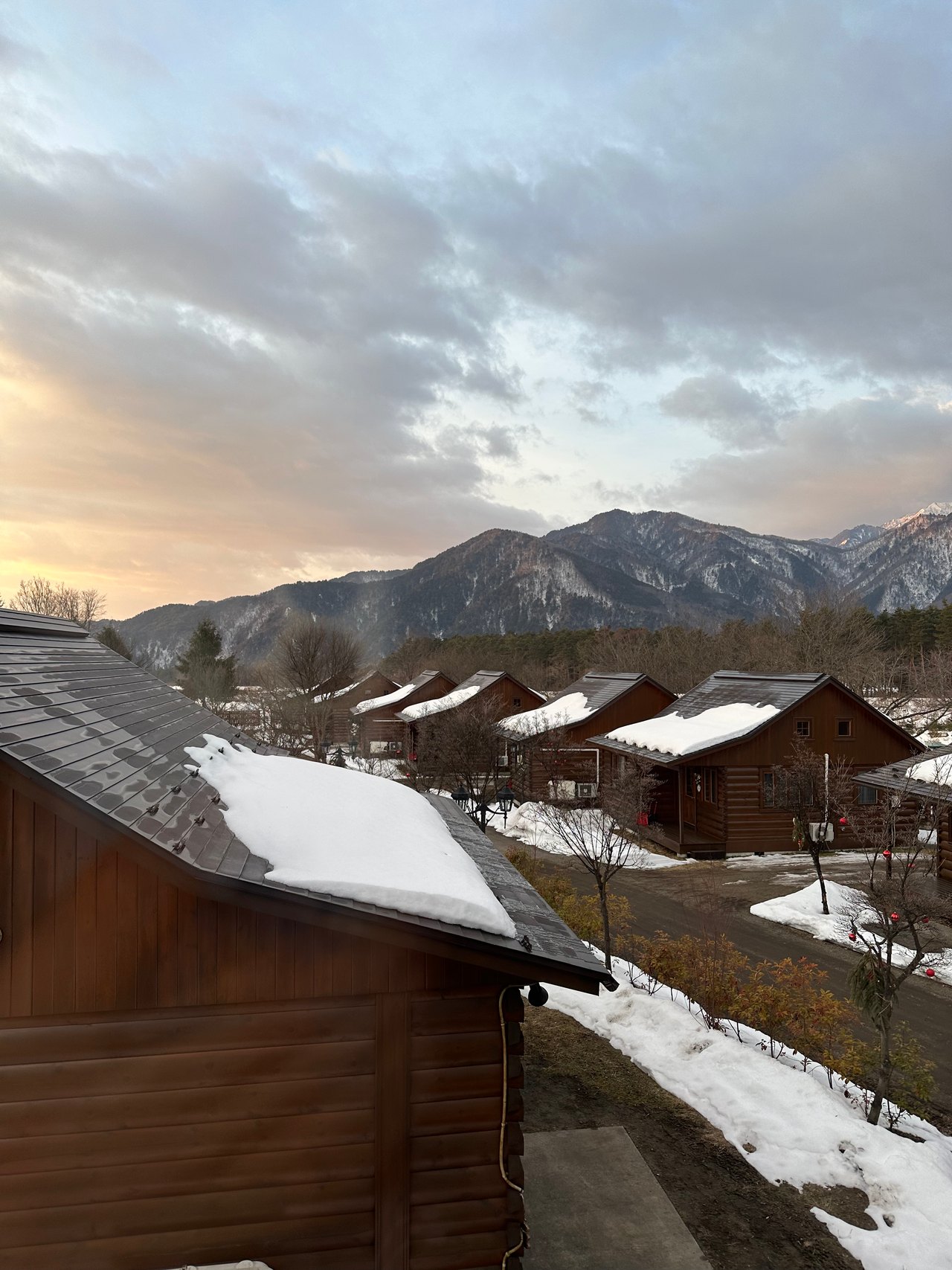 Snow-dusted cabin roofs beneath a distant mountain ridge and cloudy sky