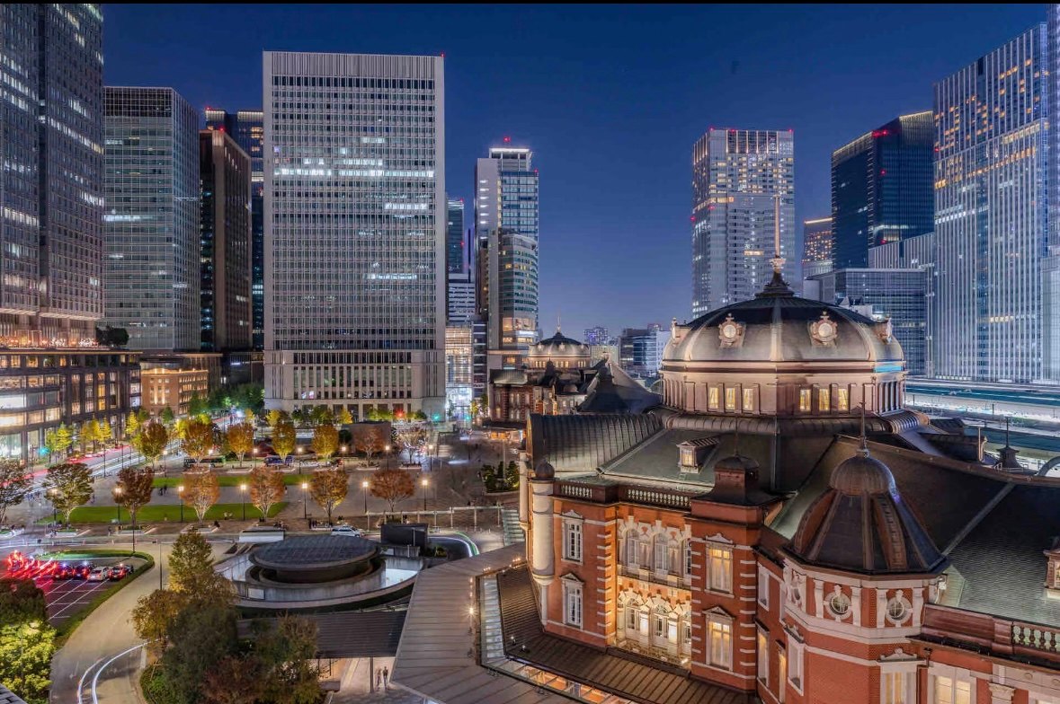 An illuminated red-brick station building stands before modern towers