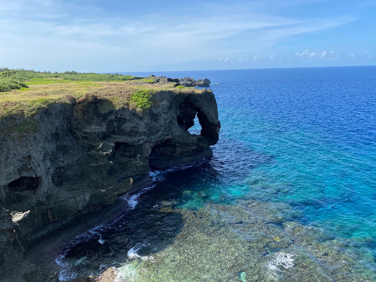 A dark rocky coast extending into clear turquoise water