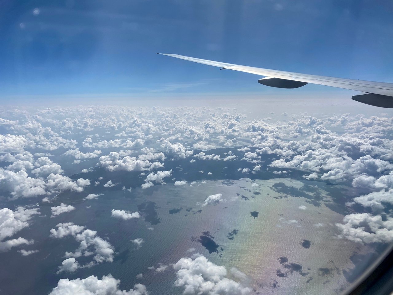 An airplane wing extends above white clouds with distant water below